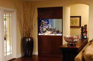 Aquarium within a wall in a dark wood casing with giant vase holding dry timber and other decorative items on a hutch